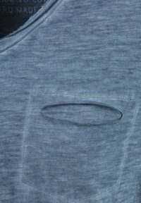 Nahaufnahme eines blauen gestrickten T-Shirts mit einer kleinen rechteckigen Brusttasche mit horizontaler Öffnung.