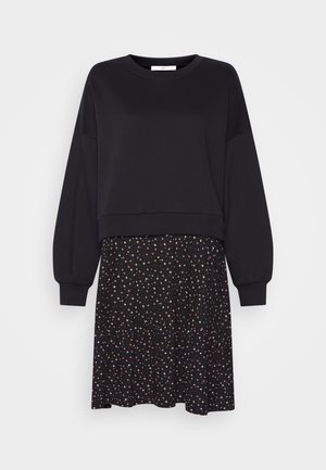 Sweat-shirt noir à manches longues associé à une jupe noire avec un petit motif floral multicolore et un ourlet volanté.