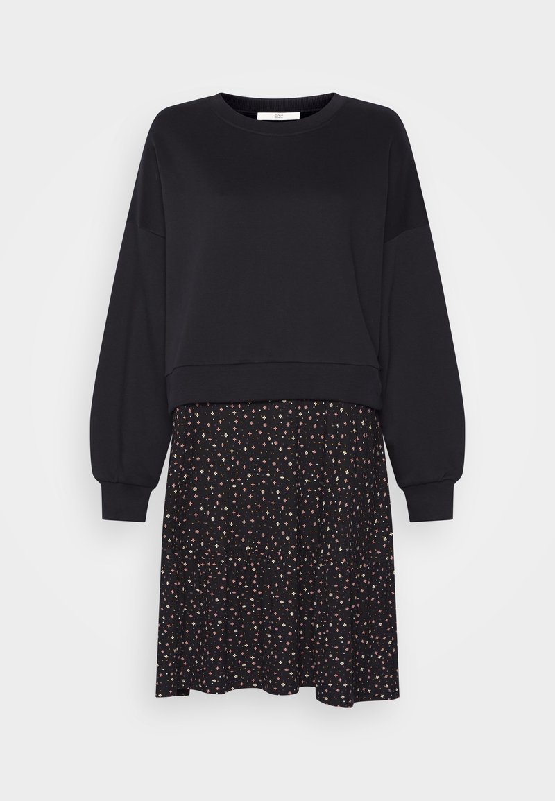 Sweat-shirt noir à manches longues associé à une jupe noire avec un petit motif floral multicolore et un ourlet volanté.