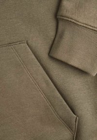 Tejido de sudadera verde oliva con puños acanalados y detalle de bolsillo, con una textura suave y costuras marcadas.