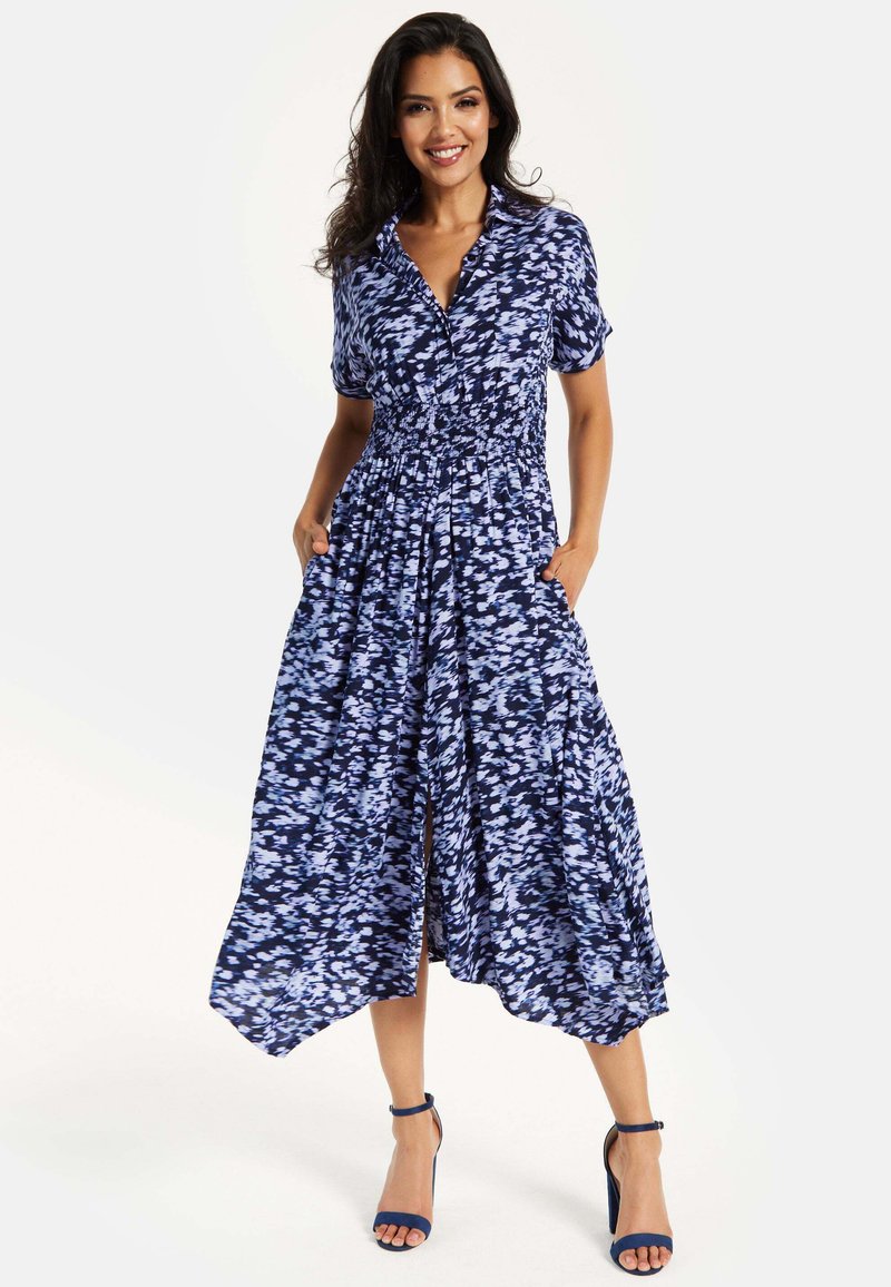 Navy and light blue patterned dress with short sleeves, smocked waist, pockets, and a flowy silhouette, paired with matching heels.