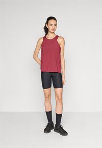 Canottiera sportiva bordo, pantaloni shorts neri con motivo, calze nere e scarpe scure. Il tessuto è leggero; la canottiera ha una vestibilità ampia e un design a racerback.