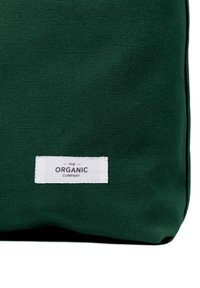 Tamnozeleni torba od teksturirane tkanine s bijelom etiketom na kojoj piše "THE ORGANIC COMPANY" u crnoj boji. Jednostavnog pravokutnog oblika.