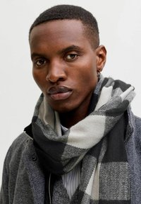 Abrigo de mezcla de lana gris combinado con una bufanda a cuadros en negro y gris, que presenta una textura suave y un diseño en capas. La bufanda se enrolla alrededor del cuello.