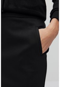 Jupe noire au tissu lisse, dotée de poches latérales et d'une coupe ajustée. La taille est finie avec un design subtil et épuré.