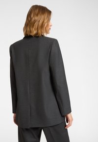 Blazer ajusté gris foncé, en tissu texturé, avec une coupe longue, des épaules structurées et une fente centrale à l'arrière.