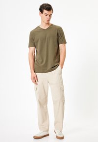 Olivenfärgad bomull t-shirt med v-ringning, tillsammans med beige cargobyxor med flera fickor och en avslappnad passform. Vita sneakers fulländar looken.