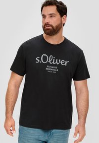 Mustmustriistest t-särk, millel on ümar kaelus, hall "s.Oliver" logo ja tekst "ELEVATED ESSENTIALS SINCE 1969", lühikesed varrukad.