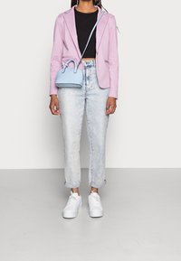 Vaaleanpunainen bleiseri mustan lyhyen t-paidan päällä, yhdistettynä vaaleisiin farkkuihin, joiden lahkeet on käännetty, ja valkoisiin tennareihin. Pieni vaaleansininen käsilaukku.