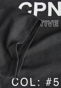 Sort T-shirt med korteærmer, der har hvid tekst: "CPN" og "COL: #5". Stoffet er glat, med synlige syninger og en blød tekstur.