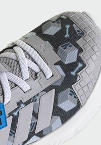 Athletic shoe featuring a gray patterned mesh upper with blue and gray accents, textured overlays, and white, flat laces.