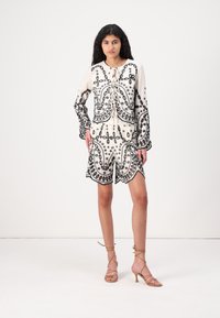 White embroidered outfit featuring a long-sleeve top with black patterns and a matching shorts design, accented with a tie detail.