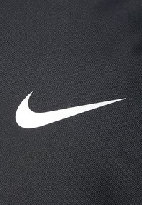 Tissu noir texturé avec un logo swoosh Nike blanc proéminent. Le design présente une surface lisse et des détails de couture.