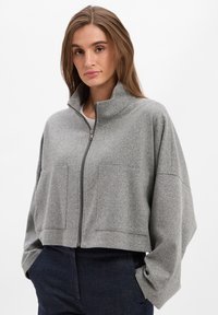 Graue, kurz geschnittene Jacke mit hohem Kragen, ausgestattet mit einem Frontreißverschluss, zwei großen Taschen und einem weich strukturierten Stoff.