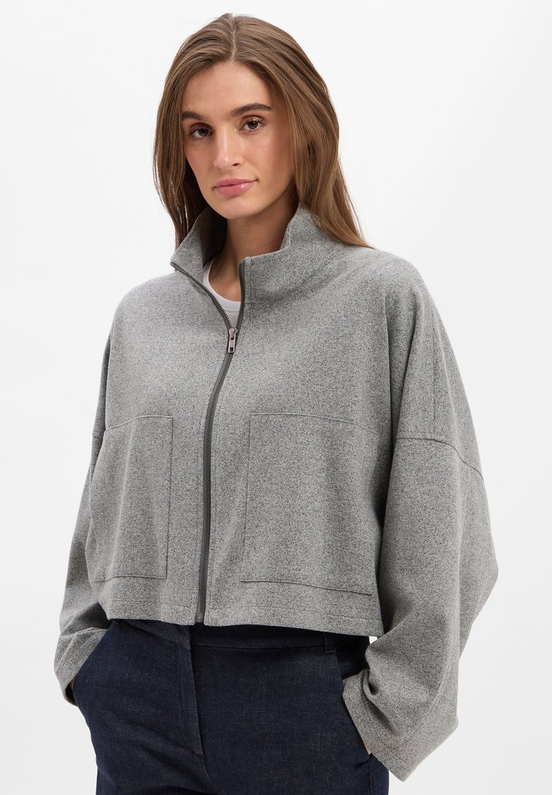 Graue, kurz geschnittene Jacke mit hohem Kragen, ausgestattet mit einem Frontreißverschluss, zwei großen Taschen und einem weich strukturierten Stoff.