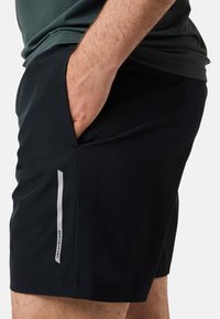 Svarta träningsshorts i lättviktig tyg, med en sidoficka och en vit vertikal rand med logotyp.