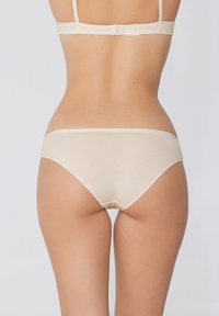 Mutande beige con una texture liscia, design a vita bassa e copertura minima. L'elastico è semplice, senza motivi o decorazioni visibili.
