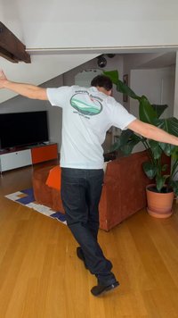 Άτομο με λευκό T-shirt Rip Curl Surfing και σκούρο τζιν ισορροπεί στο ένα πόδι με τα χέρια απλωμένα σε ένα σαλόνι.