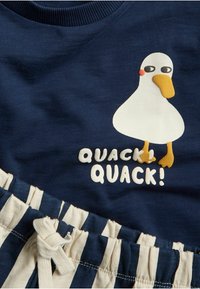 Laiva sininen paita, jossa on kumirapun kuva ja teksti "QUACK! QUACK!"; puuvillamateriaali; yhdistetty raidallisiin puuvillashortseihin, joissa on naru.