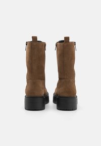 Bottines en suède marron avec une finition texturée, semelles en caoutchouc noir et fermetures éclair sur le côté. Présente un design minimaliste et un talon plat.