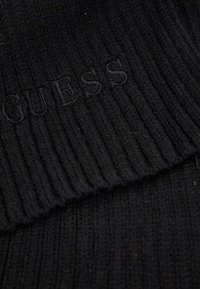 Tessuto a maglia a coste nero con logo "GUESS" ricamato in modo discreto con filo nero abbinato.