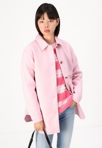 Light pink wool blend jacket with a button closure, side pockets, and a collared neck, layered over a pink striped knit sweater.