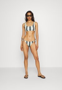 Conjunto de biquíni com um top de decote redondo e parte de baixo atada de lado, apresentando um padrão ondulado em azul claro e preto. O material parece suave e extensível.