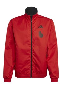 Veste légère rouge avec une fermeture éclair noire, un col montant et des poignets élastiques. Comprend des logos noirs sur la poitrine gauche et le haut du bras.