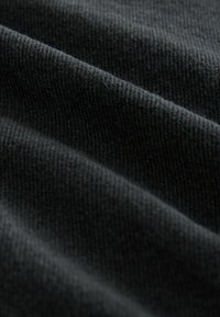 Sort tekstureret stof med synlige ribber og folder, blødt strikket materiale, der viser fine fibre og en glat overflade.