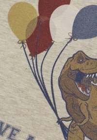 Lichtgrijze stof met een grafisch ontwerp van een dinosaurus die blauwe, rode, gele en witte ballonnen vasthoudt, met een gestructureerd, speels ontwerp.