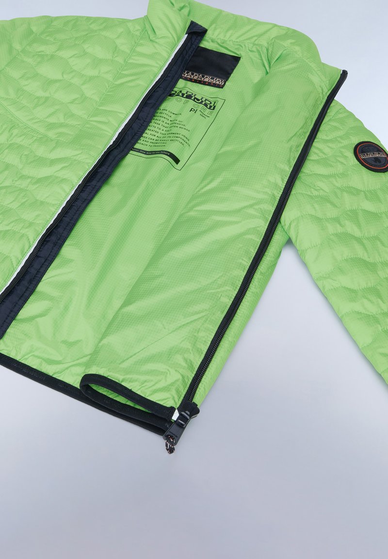 Chaqueta acolchada verde con cremallera y ribetes negros, que cuenta con una etiqueta interior y un parche en la manga. Textura ligera y suave.