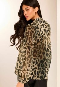 Durchsichtige Bluse mit langen Ärmeln im Leopardenmuster in Grün-, Braun- und Schwarztönen; weiche Textur und eine geraffte Rückennaht.