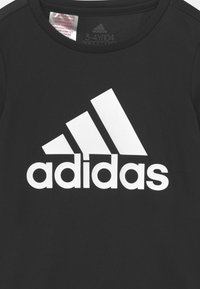 Camiseta atlética negra con un gran logotipo blanco de Adidas en el pecho. Fabricada con un tejido suave y transpirable. Mangas cortas y escote redondo.