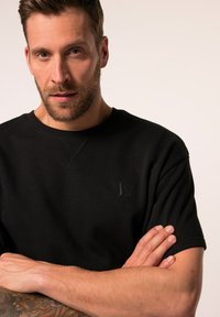 Sort bomulds sweatshirts med rund hals, korte ærmer og diskret logo detalje på brystet. Glat tekstur med en afslappet pasform.