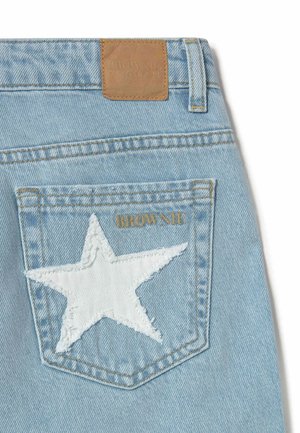 Bolsillo trasero de vaqueros de mezclilla azul claro con parche de estrella blanca y bordado en texto dorado "BROWNIE", etiqueta de cuero marrón claro de la marca sobre la cintura.