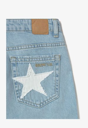 Light blue denim jeans back pocket with white star patch and gold "BROWNIE" text embroidery, tan leather brand label above waistband.