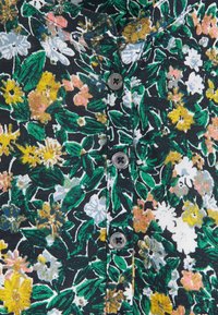 Blommig skjorta med svart bakgrund, med ett tätt mönster av gula, vita och rosa blommor, samt en enda grå knappdetalj.