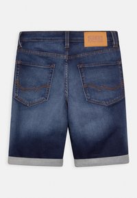 Pantalones cortos de mezclilla con un degradado azul medio, dobladillo enrollado y costuras naranjas. Presenta dos bolsillos traseros y un parche de cuero marrón claro con el logo.