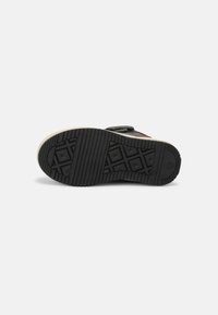 Suola in gomma nera con motivo di grip texturizzato, con un bordo beige e un'impronta di branding, progettata per aderenza e durata.
