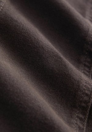 Brunt tekstureret stof med en fin vævning, der viser subtile bølger og syninger langs kanten, hvilket indikerer blødhed og holdbarhed.