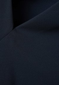 Tissu bleu marine foncé avec un tissage texturé subtil, montrant un pli diagonal créant des ombres douces à la surface.