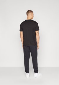 Zwarte korte mouwen t-shirt, gemaakt van katoen, met een casual pasvorm. Gecombineerd met donkergrijze joggingbroek, met elastische boorden, en witte sneakers.