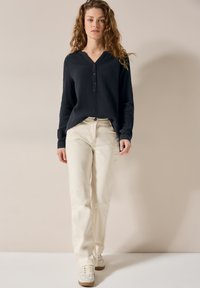 Marineblå knapp-up, struktureret top med lange ærmer; sat sammen med lysebeige, løstsiddende bukser og hvide sneakers med brune såler.