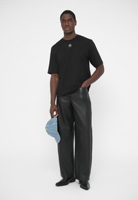 Juoda trumpomis rankovėmis marškinėliai su apskritimu logotipu, derinami su plačiomis juodomis odinėmis kelnėmis. Rankose laikoma šviesiai mėlyna džinsinė kepurė.