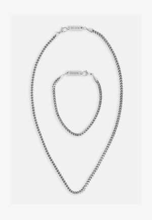 Sølvfarget kjede og armbåndssett med sammenkoblede lenker, strømlinjeformet design og metallkomponenter med "ICON" gravering.