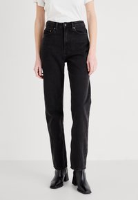 Höga svarta jeans i denim med rak ben, med en knappstängning och framfickor, kombinerat med svarta klackboots i ankelhöjd.