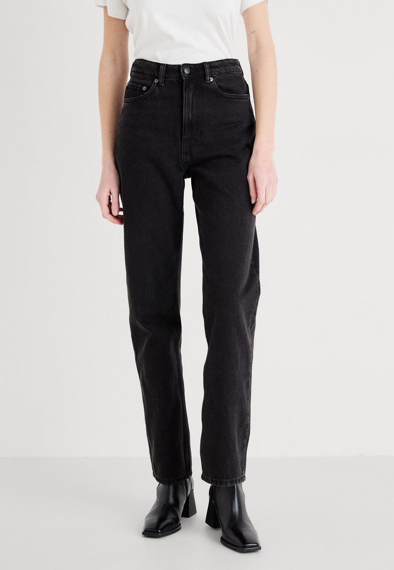 Höga svarta jeans i denim med rak ben, med en knappstängning och framfickor, kombinerat med svarta klackboots i ankelhöjd.