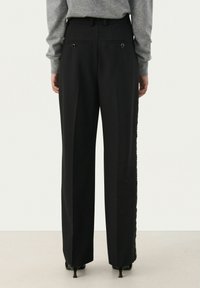 Zwarte slim fit broek met rechte pijpen, voorzien van twee achterzakken met ronde metalen accenten en een gladde stoftextuur.