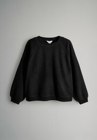 Musthave musta pikaeeline fliispullover, millel on ümar kaelus ning ribakujulised mansetid ja kant, ripub heledat halli tausta vastas.