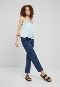 Camisola din satin de culoare albastru deschis, cu bretele ajustabile, purtată cu blugi drepti de culoare albastru închis și sandale cu brățări negre. Design simplu și croială casual.